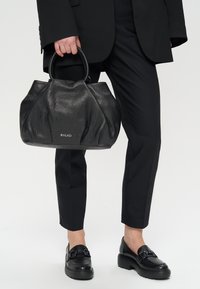 Czarna skórzana torebka z teksturowanym wykończeniem, zaokrąglonymi uchwytami i plisowanym wzorem. Logo marki widoczne z przodu.