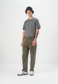 Gray short-sleeve t-shirt, olive green textured jeans, and white sneakers with black accents. Accessories include a navy bucket hat.