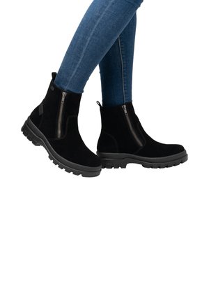 Black suede ankle boots with a zipper on the outer side, featuring a thick rubber sole and rounded toe. Worn with blue jeans.