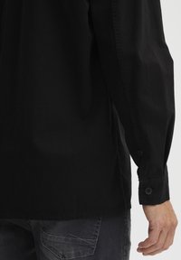 Zwarte lange mouw shirt van katoen, met een dichtgeknoopt manchet, zijsleuven en een ruime pasvorm. Gedragen met grijze, gestructureerde broek.