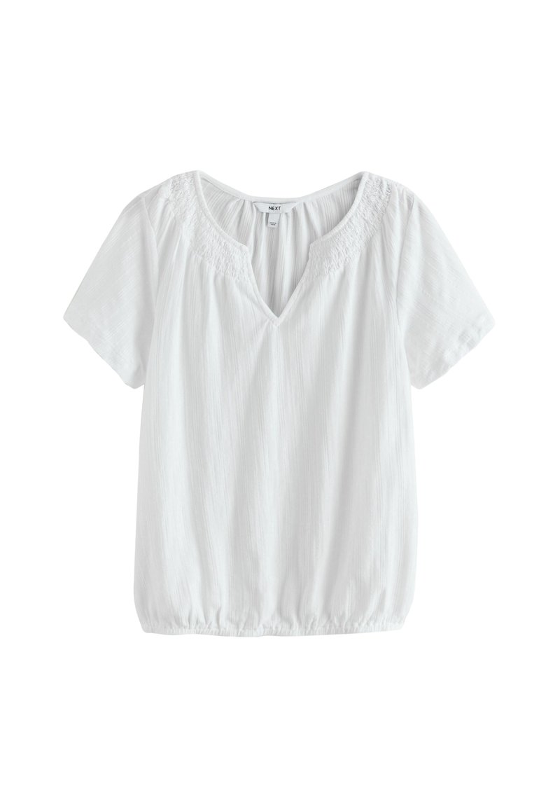 Blouse blanche à manches courtes avec un col en V, un ourlet élastique et des détails délicats en dentelle autour du col.