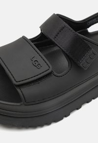 Sorte sandaler med justerbare stropper med borrelås, en polstret såle og en teksturert fotseng. Hevet profil med en glatt finish.