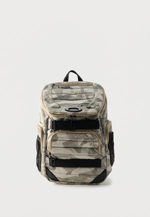 Terepmintás hátizsák több cipzáras rekesszel, fekete pántokkal, hálós oldalzsebekkel és egy felső hordozófogantyúval, fehér háttéren.