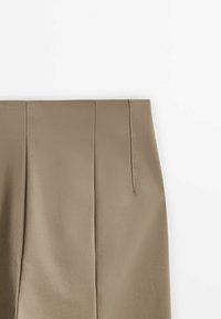 Jupe beige taille haute avec un pli sur le devant et une fermeture éclair latérale sur fond blanc.