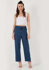 Biely priliehavý crop top s štvorcovým výstrihom, skombinovaný s voľnými, tmavomodrými nohavicami so šnúrkami a textúrovanou látkou. Sandále s viacfarebnými páskami.