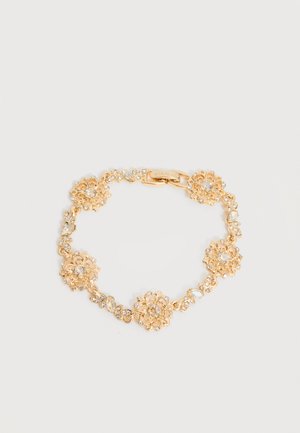 Zlata cvetlična zapestnica s prozornimi dragimi kamni in pravokotnim zaponkom na svetlo sivi podlagi.