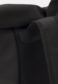 Černý batoh s rolovacím víkem, texturovanou síťovinou a hladkým syntetickým materiálem se zesílenými švy a akcenty.