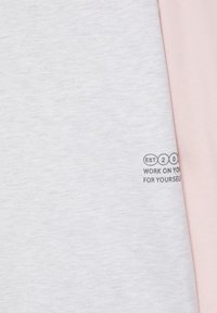 Gros plan de deux t-shirts pliés, l'un gris clair avec un texte partiel, l'autre rose doux, superposés sur une surface plane.