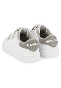 Zapatillas blancas con acentos de gamuza gris, que cuentan con una correa de velcro y el texto "QUE TENGAS UN BUEN DÍA" en el talón. Material suave, diseño minimalista.