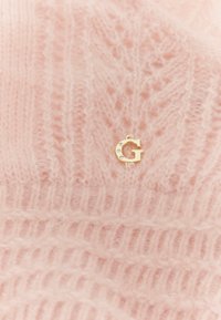 Pehme roosa kootud kangas ribade ja pitsimustritega, kaunistatud väikese kuldse tähega "G", mille sees on kätketud kristallid.