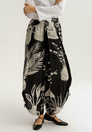 Czarna spódnica w wzory z białymi kwiatowymi i botanicznymi motywami, o zwiewnym kroju i regulowanym sznurkiem w talii.