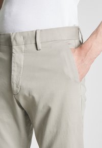 Ljusbeige byxor tillverkade i slätt tyg, med sidofickor, slim fit-design och platt front med subtila sömmar.