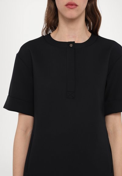 Fekete ruha rövid ujjakkal, kerek nyakkivágással és gombos záródással. Két oldalsó zsebet és texturált varrás részletet tartalmaz.