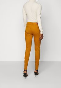 Senapsgula skinny jeans i stretchmaterial med hög midja, med två bakfickor och bälteshällor, kombinerade med en figurnära krämfärgad topp.