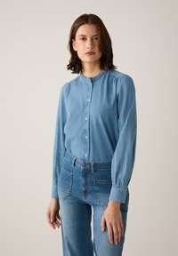 Lichtblauwe denim shirt met een ronde halslijn, knopen aan de voorkant, lange mouwen en geplooide details bij de schouders. In combinatie met bijpassende jeans.