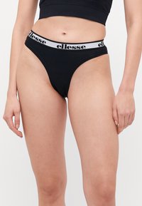 Fekete tanga fehér, kontrasztos derékpánttal, amelyen fekete "ellesse" logó található. Simaságot és minimalista designt kínáló anyag.