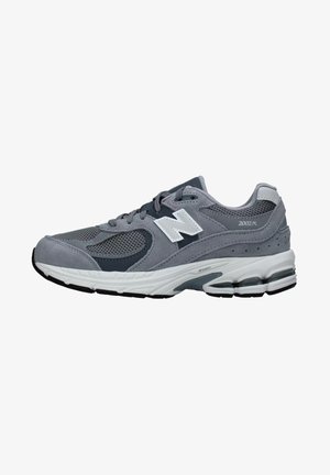 Zapatilla deportiva gris con material de malla y ante, que presenta un logo blanco, acentos oscuros, una suela acolchada y soporte para el talón moldeado.