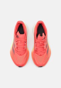 Svijetlo koraljne trkačke cipele s mrežastim gornjim dijelom, crnim akcentima i bijelim potplatima. Imaju jastučić oko gležnja i teksturirani grip na potplatu.