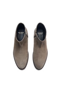 Botas de tobillo de ante en gris con una textura suave, cremallera lateral y diseño de punta redonda. Logo de la marca exhibido en el forro interior.
