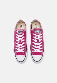 Para jasnoróżowych niskich trampków Converse All Star z białymi sznurówkami i gumowymi noskami na białym tle.