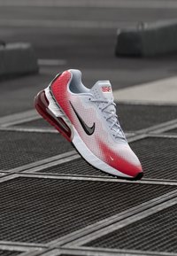 Le scarpe Nike Air Max presentano una tomaia bianca con gradiente rosso, accenti neri, una superficie testurizzata e un'unità air visibile nel tallone.