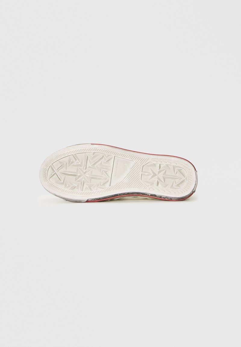 Suela de zapatilla blanca con patrones de relieve geométricos y la marca "DIESEL", vista desde abajo sobre un fondo blanco liso.