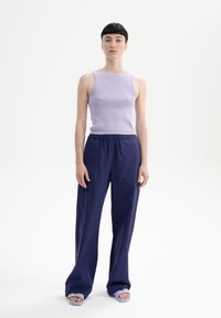 Lila aansluitende tanktop, marineblauwe losse broek met elastische tailleband, en lichtpaarse platte sandalen. Eenvoudig ontwerp zonder zichtbare patronen.