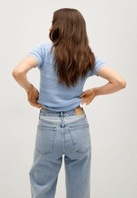 Haut tricot à manches courtes bleu clair avec un motif texturé, associé à un jean en denim délavé taille haute et à un design minimaliste.