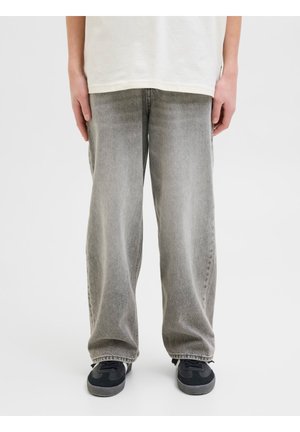 Personne portant un jean gris ample, des baskets noires et une chemise blanche, les mains détendues le long du corps.