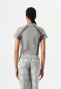Maglietta grigia tagliata con maniche corte, cuciture in contrasto e design dello yoke strutturato, abbinata a jeans dritti sbiaditi di colore blu chiaro.