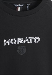 Sudadera negra con un logo de león bordado texturizado y un texto impreso en blanco que dice "MORATO" en diferentes grosores de línea.