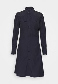 Abito blu navy con maniche lunghe, bottoni e colletto, caratterizzato da dettagli arricciati. Due tasche sul petto e orlo curvo con bordi scallop.
