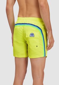 Costumi da bagno giallo brillante con accenti a strisce blu e verdi, vita elastica e una tasca posteriore con un patch logo.