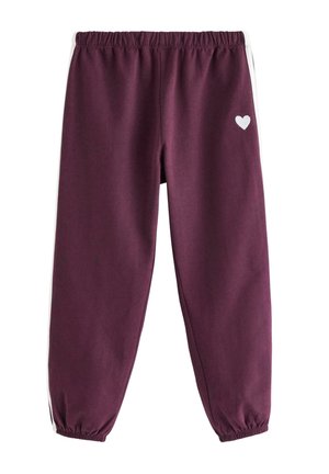 Barn med krøllet hår iført en hvid blomsterlangærmet skjorte, bordeaux joggingbukser med hvide striber og matchende bordeaux sneakers.
