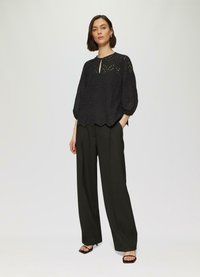Zwarte blouse met geborduurde details en een ronde halslijn, gecombineerd met zwarte high-waisted wijde broek en open teen zwarte hakken.