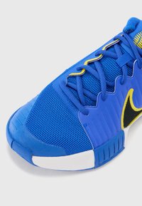 Blaues Sportschuh-Modell mit einem Obermaterial aus Mesh, gelben Akzenten, strukturiertem Zehenbereich und charakteristischem schwarzen Logo. Verfügt über Schnürsenkel und einen gepolsterten Schaft.