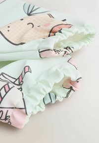 Világos menta színű textil, amelyen mesefigurák stílusában készült fagylalt és ital minták láthatók, rózsaszín és fekete díszítéssel. Ráncolt mandzsetta, gumis végződéssel a ujjainál.