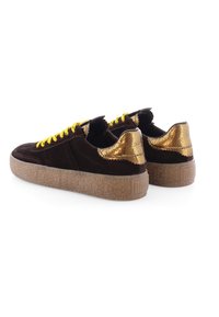 Brown suede sneakers with gold metallic accents, yellow laces, and a textured brown rubber sole. Rear view highlights unique design details.