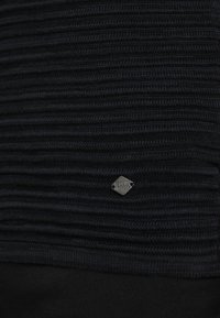 Top negru tricotat cu dungi verticale texturate, având o etichetă metalică mică în colțul de jos. Finisaj de țesătură netedă, fără modele distincte.