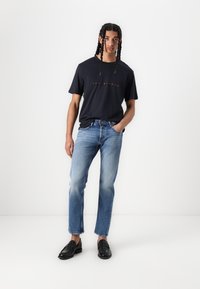 Marinblå T-shirt med rød tekst, lyseblå denim jeans og sorte loafers. Straight fit jeans og T-shirt med korte ærmer. Glat tekstur.