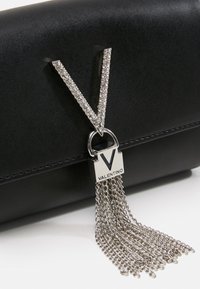 Svart läderhandväska med en silverfärgad V-formad dekoration med rhinestones, låsdetaill och hängande metalldetaljer.