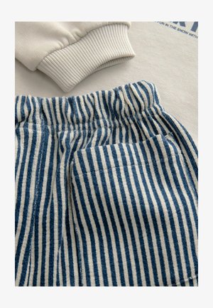 Cremefarbener Sweatshirt mit gerippten Bündchen, kombiniert mit blau-weiß gestreiften Hosen mit elastischem Bund und Taschen.