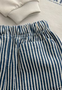 Felpa color crema con polsini a coste abbinata a pantaloni a righe blu e bianche con cintura elastica e tasca.