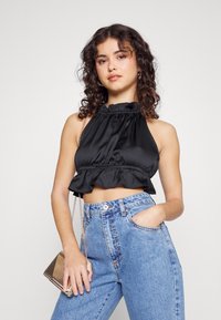 Top de halter de cetim preto com bainha em babados. Usado com jeans de ganga azul claro de cintura alta. Apresenta uma bolsa de corrente prateada.