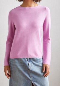 Pull en laine rose à manches longues avec un col rond, fabriqué en tissu tricot lisse. Porté par-dessus une jupe en denim clair avec une fente à l'avant.