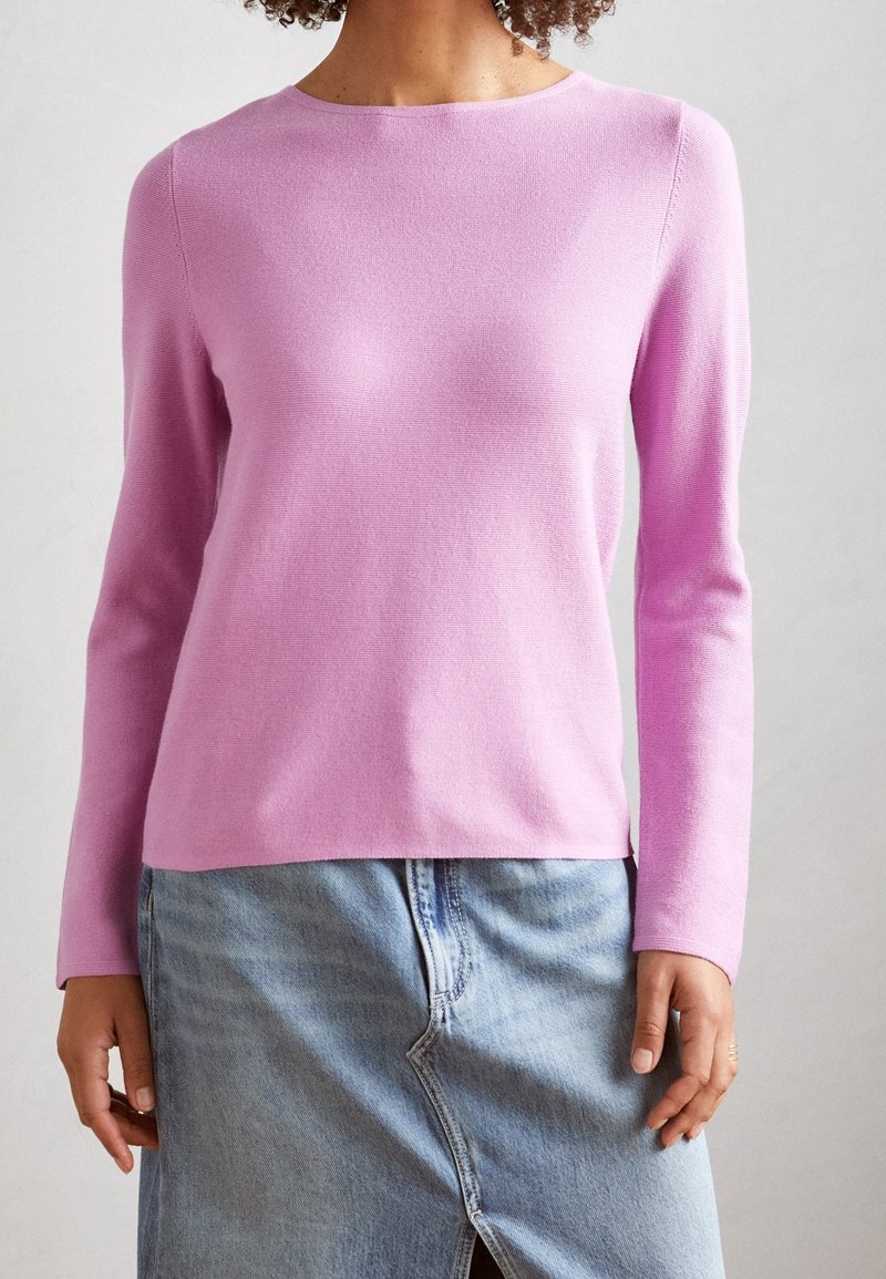 Pull en laine rose à manches longues avec un col rond, fabriqué en tissu tricot lisse. Porté par-dessus une jupe en denim clair avec une fente à l'avant.