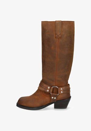 Botte haute en cuir marron avec une sangle de harnais et un anneau métallique autour de la cheville, équipée d’un petit talon empilé et d’une languette de tirage en haut.