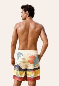 Costumi da bagno da uomo in giallo chiaro, con una scena di spiaggia decorata da palme, montagne e un tramonto. Vita elastica con motivo decorativo.