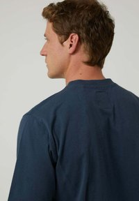 Camisa de algodón azul marino con un diseño sencillo, cuello redondeado y etiqueta de bucle en la parte trasera. Textura suave y mangas cortas.