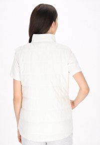 Gilet invernale bianco senza maniche con colletto alto, elegante trapuntatura orizzontale e una superficie liscia, abbinato a una camicia a maniche corte sottostante.